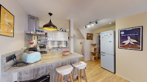 A modern kitchen with a central island, bar stools, a refrigerator, and a dining area.