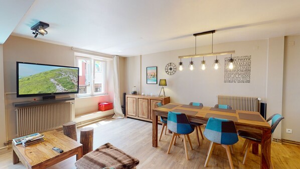A modern living room with a television, wooden furniture, a dining area, and a radiator.