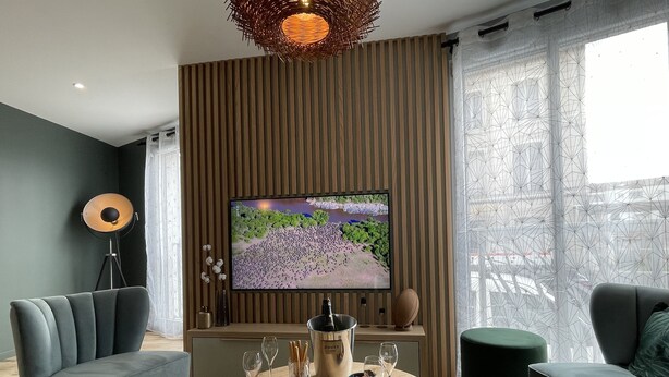 Una sala de estar moderna con un televisor de pantalla plana, dos sofás, una mesa de centro con copas de vino y una lámpara de pie.
