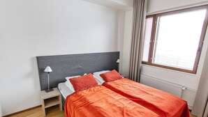 Een hotelkamer met een tweepersoonsbed, nachtkastje, lamp, raam met gordijnen en een radiator.