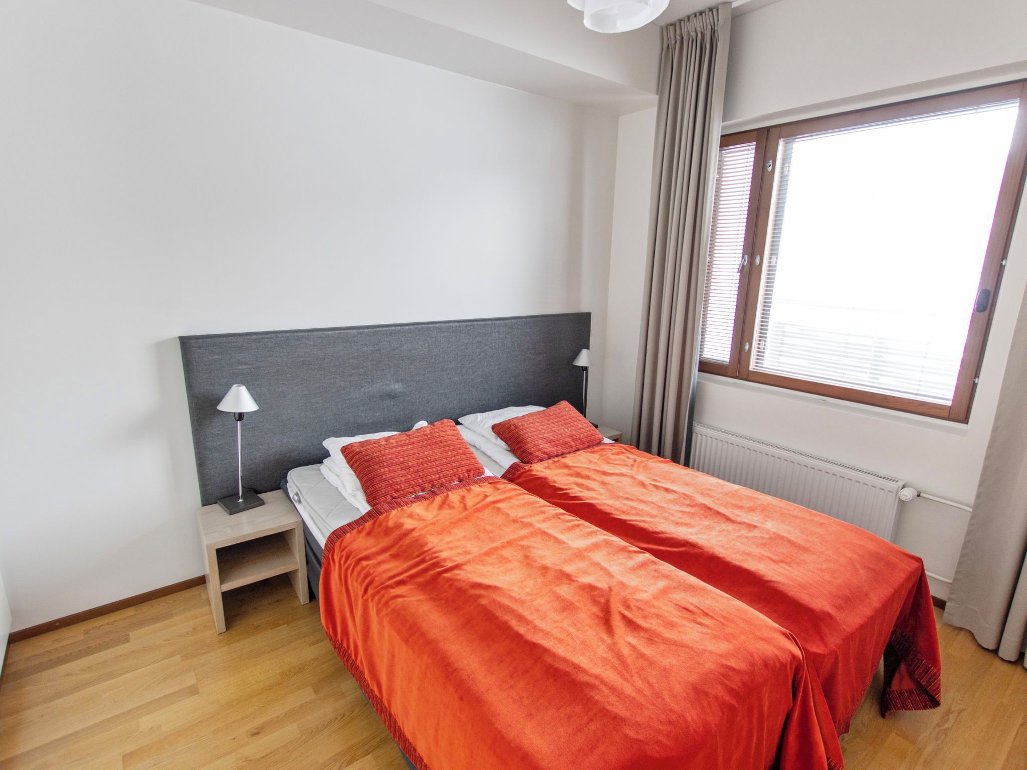 Cama de casal com roupa de cama vermelha em quarto com paredes brancas e chão de madeira.