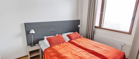 Cama de casal com roupa de cama vermelha em quarto com paredes brancas e chão de madeira.