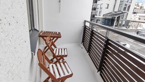 Een balkon met een houten klapstoel en een tafeltje, met uitzicht op een straat met gebouwen en geparkeerde auto's.