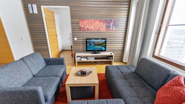 Een moderne woonkamer met twee grijze banken, een houten salontafel en een flatscreen televisie op een houten dressoir.