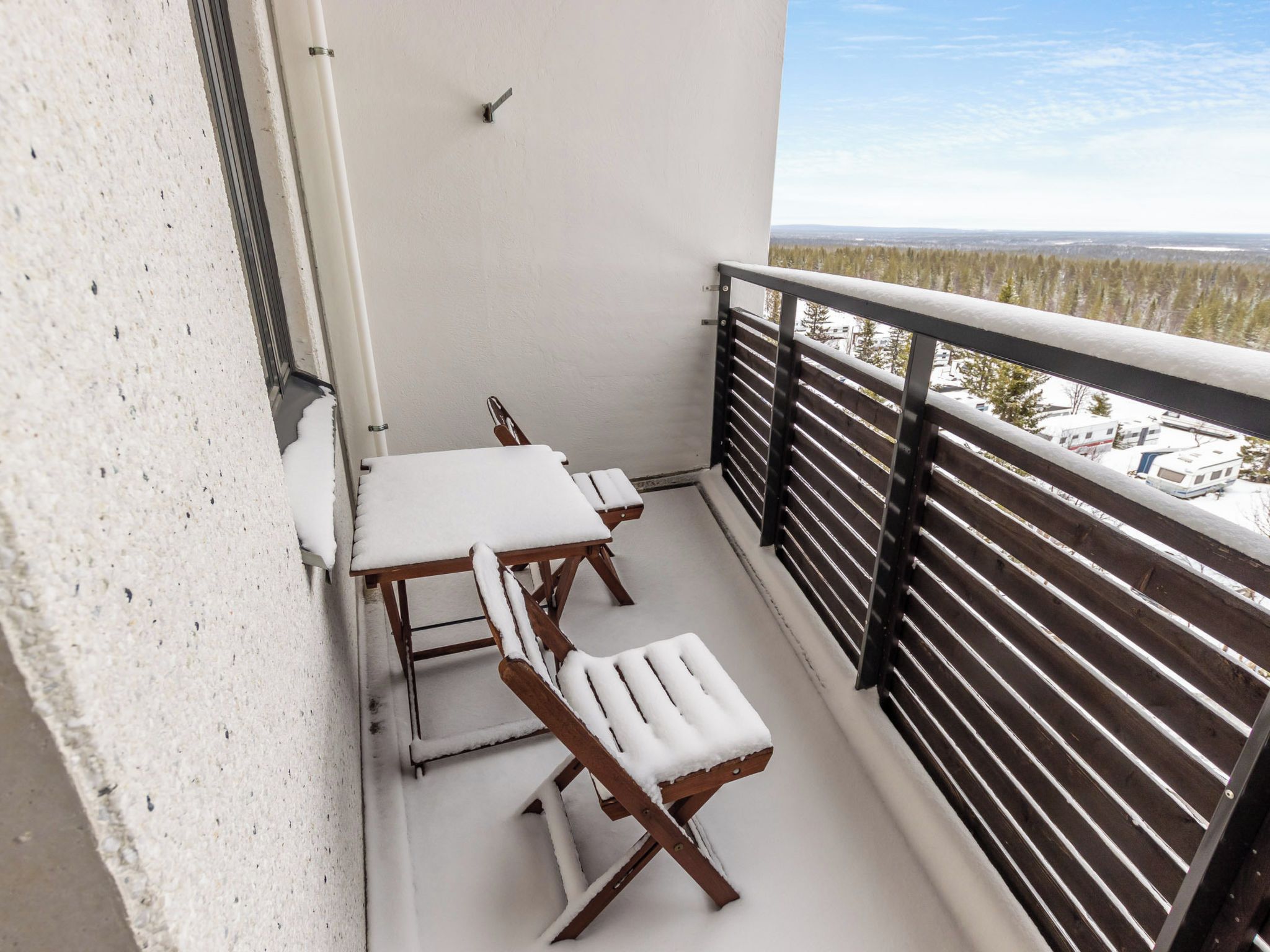 Un balcone con ringhiera bianca, un tavolo e due sedie coperte di neve.