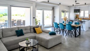 A modern living room with a grey sectional sofa, a round coffee table, and a dining area with blue chairs. - Rest for the soul by Interhome (Imotski)