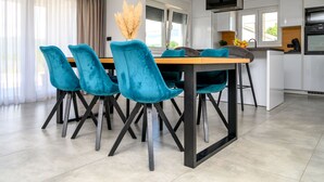 A modern kitchen with white cabinets, a black TV mounted on the wall, and a dining area with teal chairs and a wooden table. - Rest for the soul by Interhome (Imotski)
