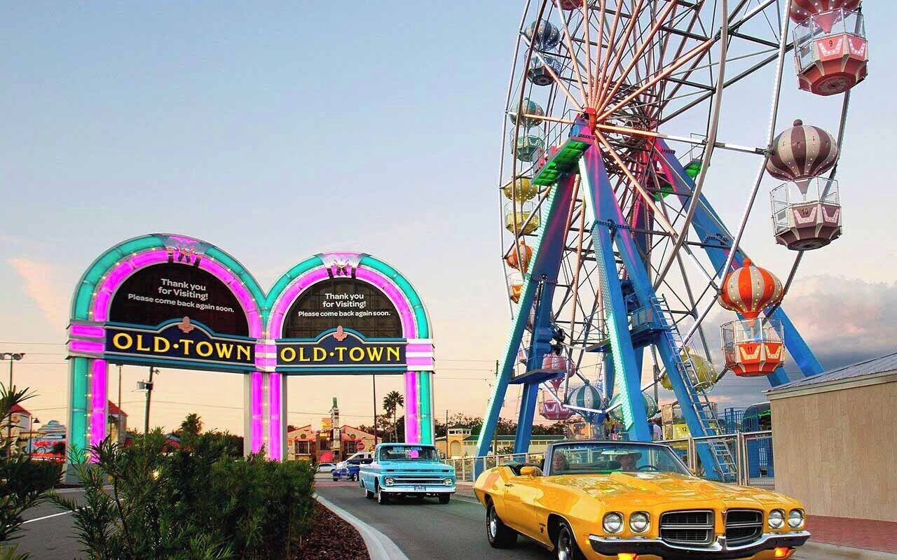 A Ferris wheel and a vintage car in front of a neon sign that reads "OLD-TOWN."