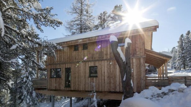 Eine hölzerne Hütte auf Stelzen in einem verschneiten Wald.