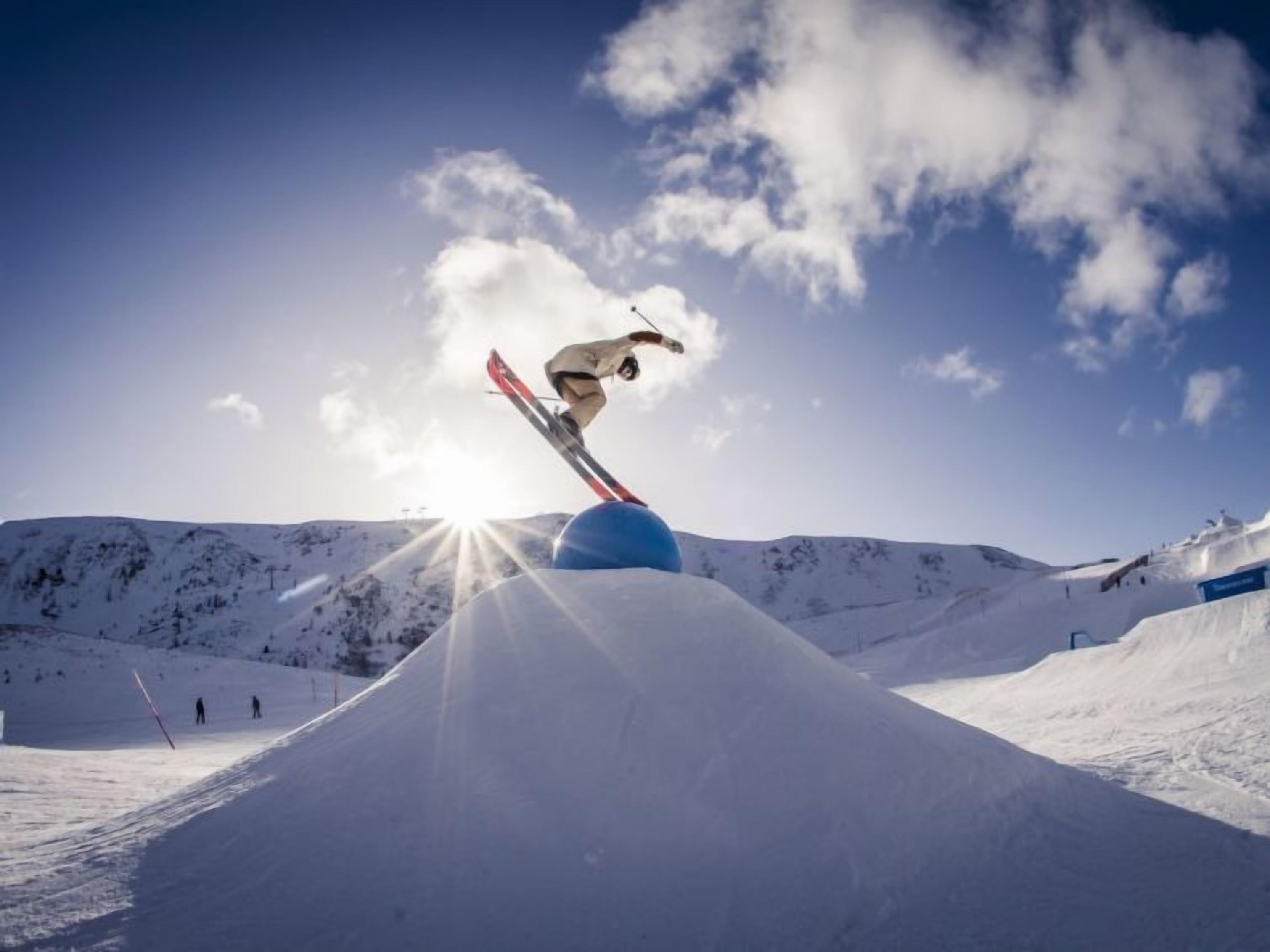 Ein Skifahrer springt über eine Schneerampe, im Hintergrund ist ein klarer Himmel zu sehen.