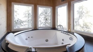 A wooden cabin with a large oval bathtub and three windows offering views of snow-covered trees. - #4 mit IR-Sauna & Sprudelwanne innen by Interhome (Turracher Höhe)