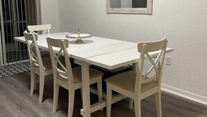 En matplats med ett vitt bord och stolar, en spegel på väggen och ett fönster med persienner.