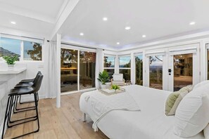 Ein modernes Schlafzimmer mit einem großen Bett, einer Sitzecke mit Sesseln und Blick ins Freie durch große Schiebetüren.