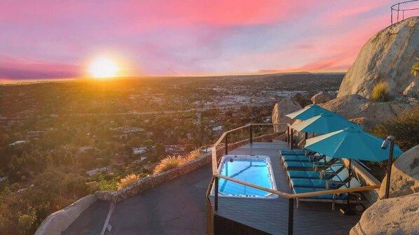 Ein Poolbereich mit Liegestühlen und Sonnenschirmen mit Blick auf eine Stadtlandschaft bei Sonnenuntergang.