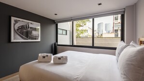 A hotel room with a large bed, two pillows with a logo, a framed picture on the wall, and a view of buildings through the window. - Wynwood House Sinaloa (Mexico City)