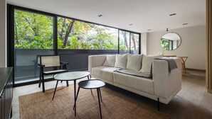 A modern living room with a large window, a sofa, two round tables, and a chair. - Wynwood House Sinaloa (Mexico City)