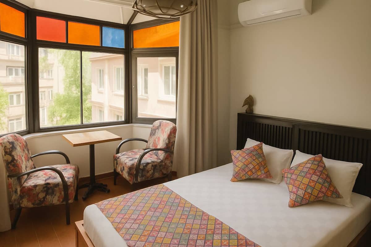A hotel room with a bed, two chairs, a small table, and a window with a view of buildings.
