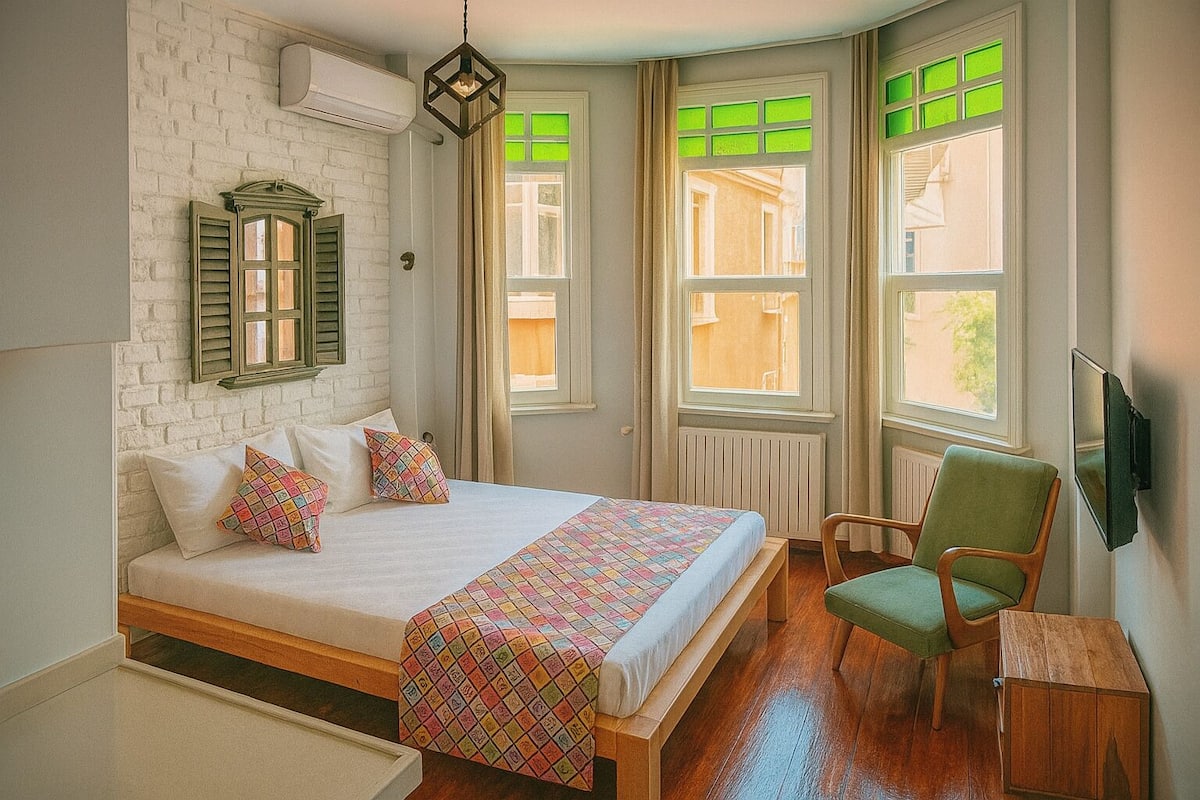 A bedroom with a bed, a chair, a TV, and a window with green shutters.