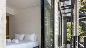 Ein modernes Schlafzimmer mit Bett, weißer Bettwäsche und Blick durch ein großes Fenster.