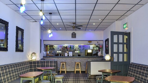 A restaurant with a bar area, seating with plaid upholstery, and a patterned floor.