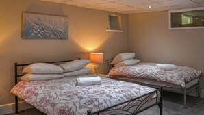 A hotel room with two single beds, a nightstand with a lamp, a painting on the wall, and a window.