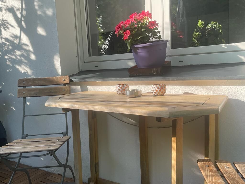 Una mesa de madera con dos tazas y platillos, una silla y una planta en maceta sobre un alféizar.