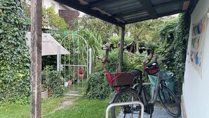 Een overdekt buitengebied met een fiets, bloempotten en een metalen hek.