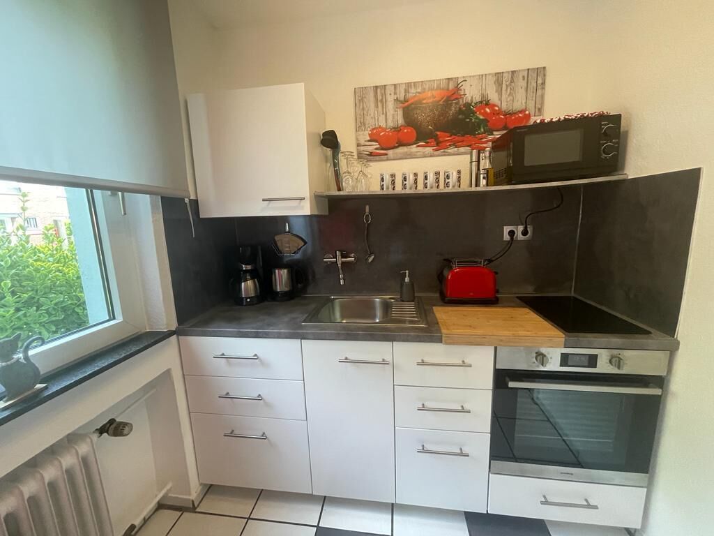 Una cucina compatta con mobili bianchi, un forno a microonde, un tostapane e un lavandino.