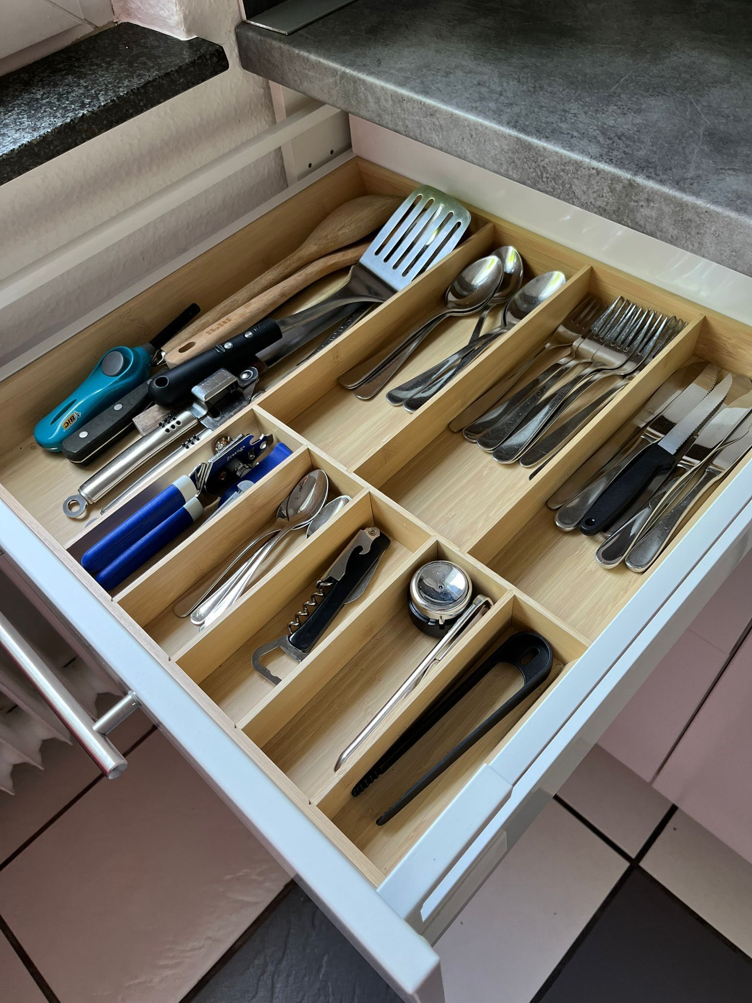 A kitchen drawer with multiple compartments containing various utensils and tools.
