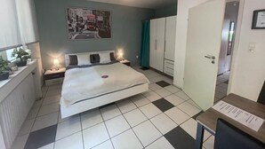 Een slaapkamer met een bed, nachtkastjes, een hanglamp, een kledingkast en een deur die naar een andere kamer leidt.