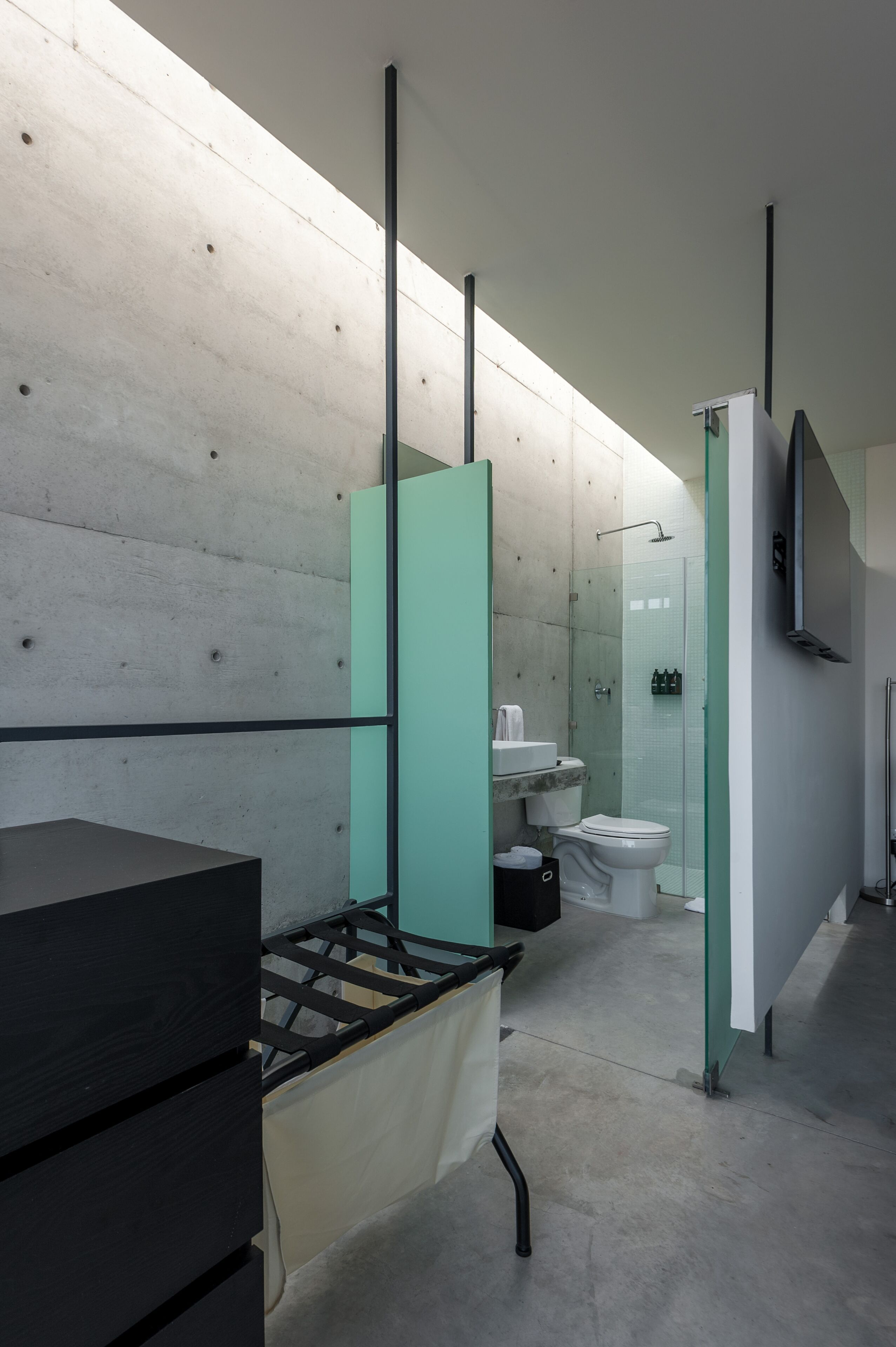 A modern bathroom with a concrete wall, a black sink, a glass shower enclosure, and a toilet.