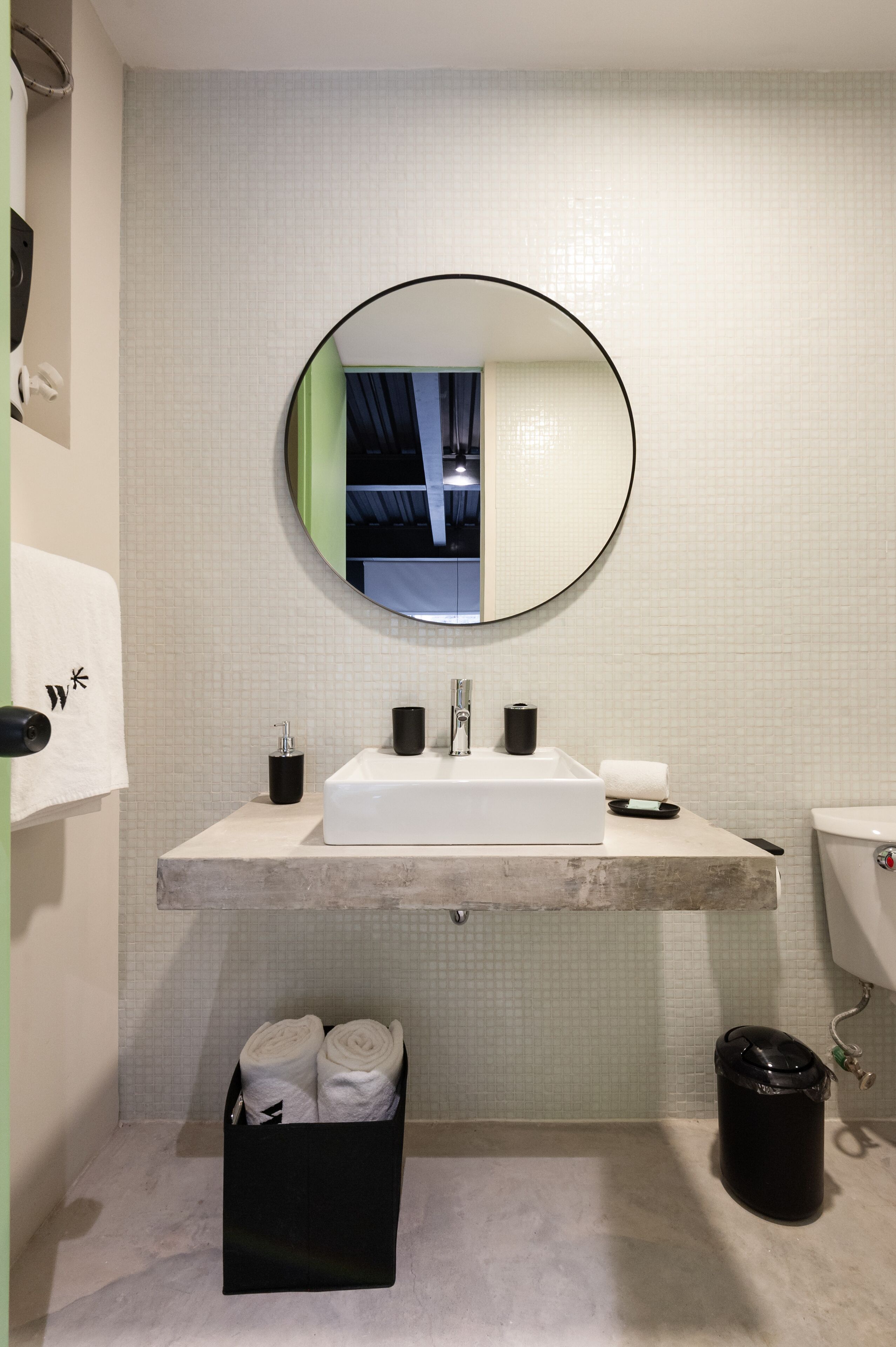 A bathroom with a round mirror, white sink, and a black trash bin.