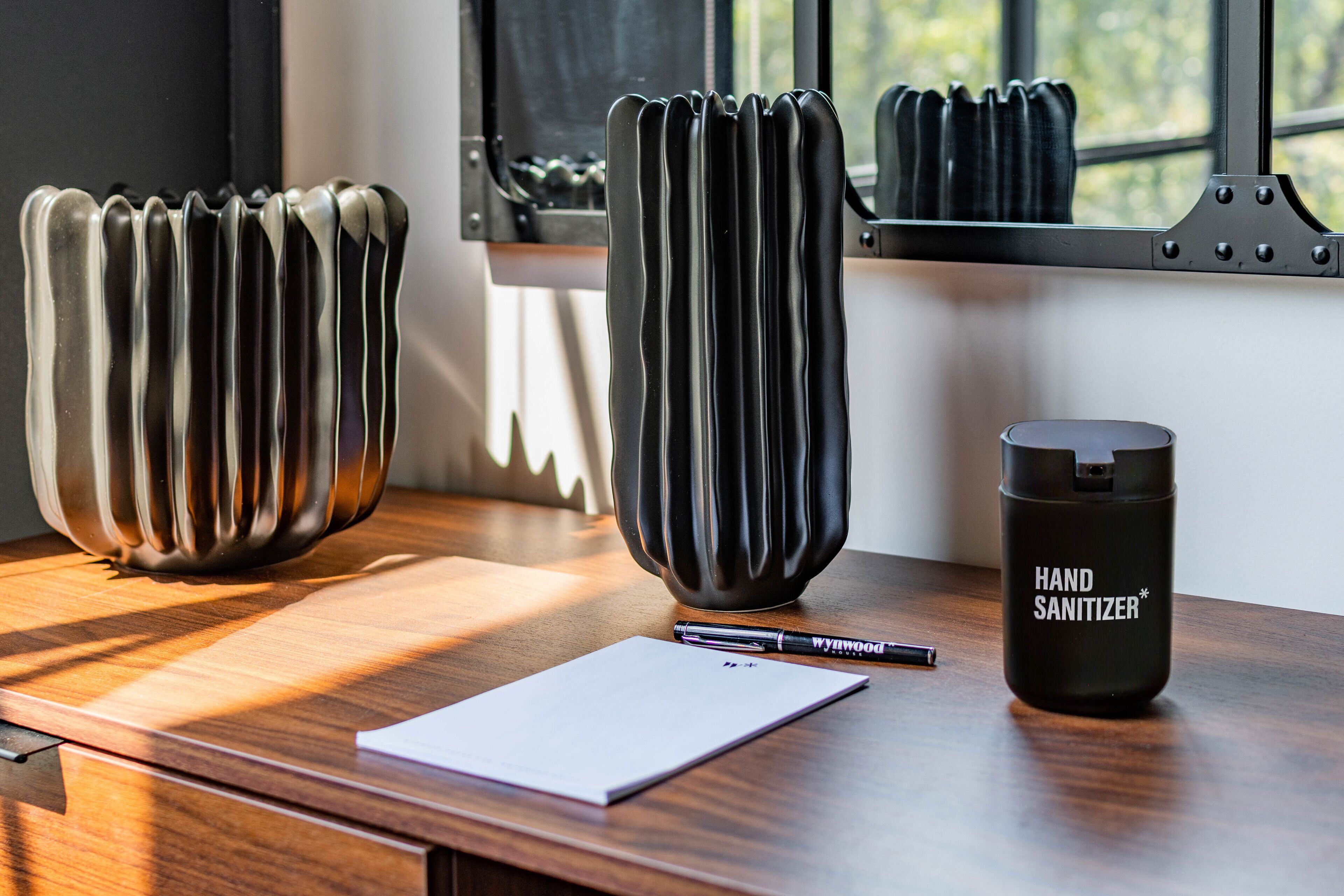 A wooden desk with a white notepad, a black pen, and a black hand sanitizer bottle.