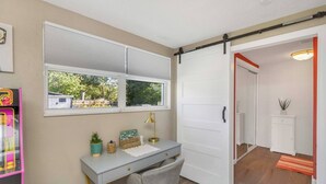 Una habitación con escritorio, silla, ventana y puerta corrediza que da a otra habitación.