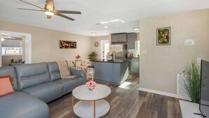 Una sala de estar moderna con un sofá gris, una mesa redonda de centro y un ventilador de techo.