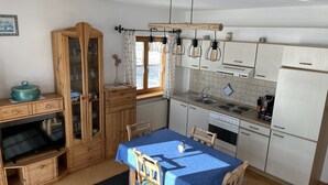 Kompakti keittiö, jossa on puiset kaapit, ruokapöytä ja sisäänrakennettu uuni.