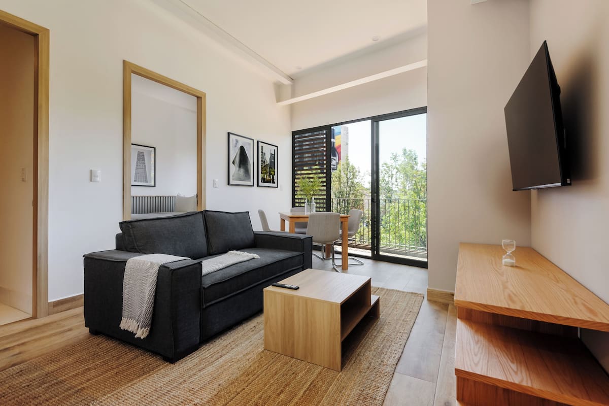 Una sala de estar moderna con un sofá negro, una mesa de centro de madera y un televisor montado en la pared.