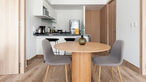 A modern kitchen with white cabinets, a stainless steel refrigerator, and a round wooden table with two chairs. - Wynwood House Londres (Mexico City)