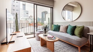 A modern living room with a grey sofa, a round mirror, and a large window with a view of buildings. - Wynwood House Londres (Mexico City)
