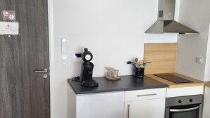 Uma cozinha moderna com cafeteira, torradeira e chaleira na bancada. Há um armário de madeira embaixo e um forno de aço inoxidável à direita.