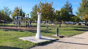 Um parque com parquinho, bancos e um monumento branco.