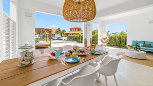 A modern dining area with a wooden table set for breakfast, white chairs, and a wicker pendant light. - Kas Azul - Water front with private pool (Kralendijk)