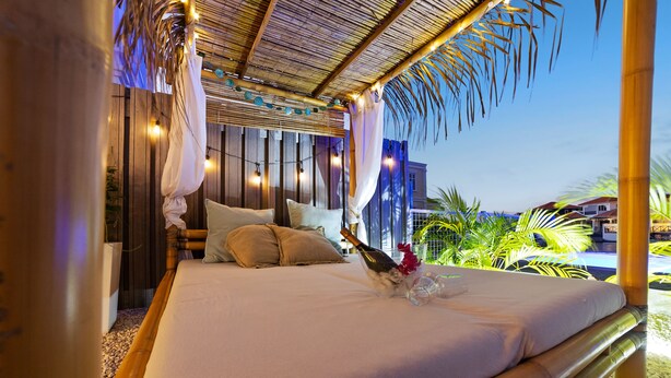 A bed with a canopy, wooden walls, and a view of a pool and palm trees. - Kas Azul - Water front with private pool (Kralendijk)