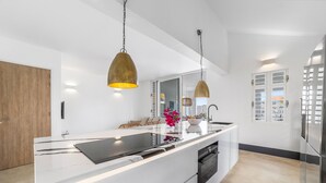 A modern kitchen with a central island, pendant lighting, and a view of the outside. - Kas Azul - Water front with private pool (Kralendijk)