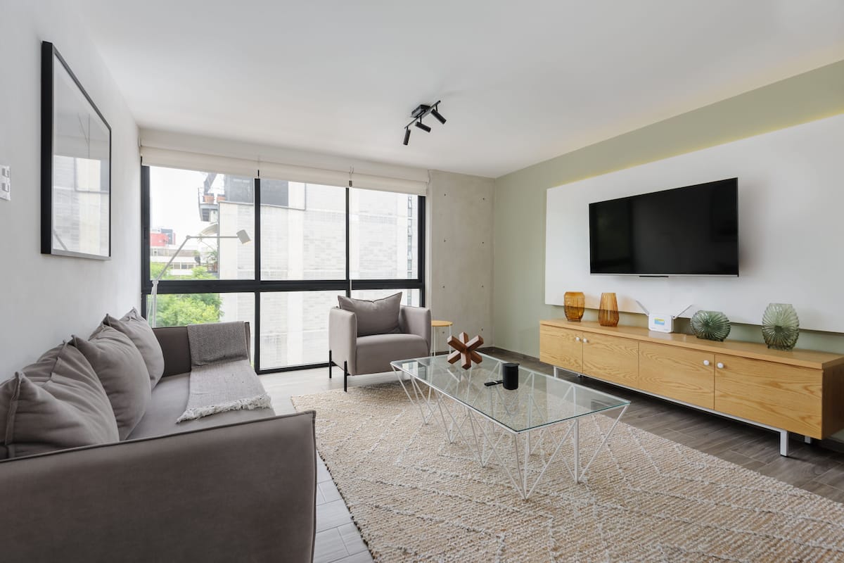 Una sala de estar moderna con un sofá, una mesa de centro de vidrio, un televisor y un mueble de madera.