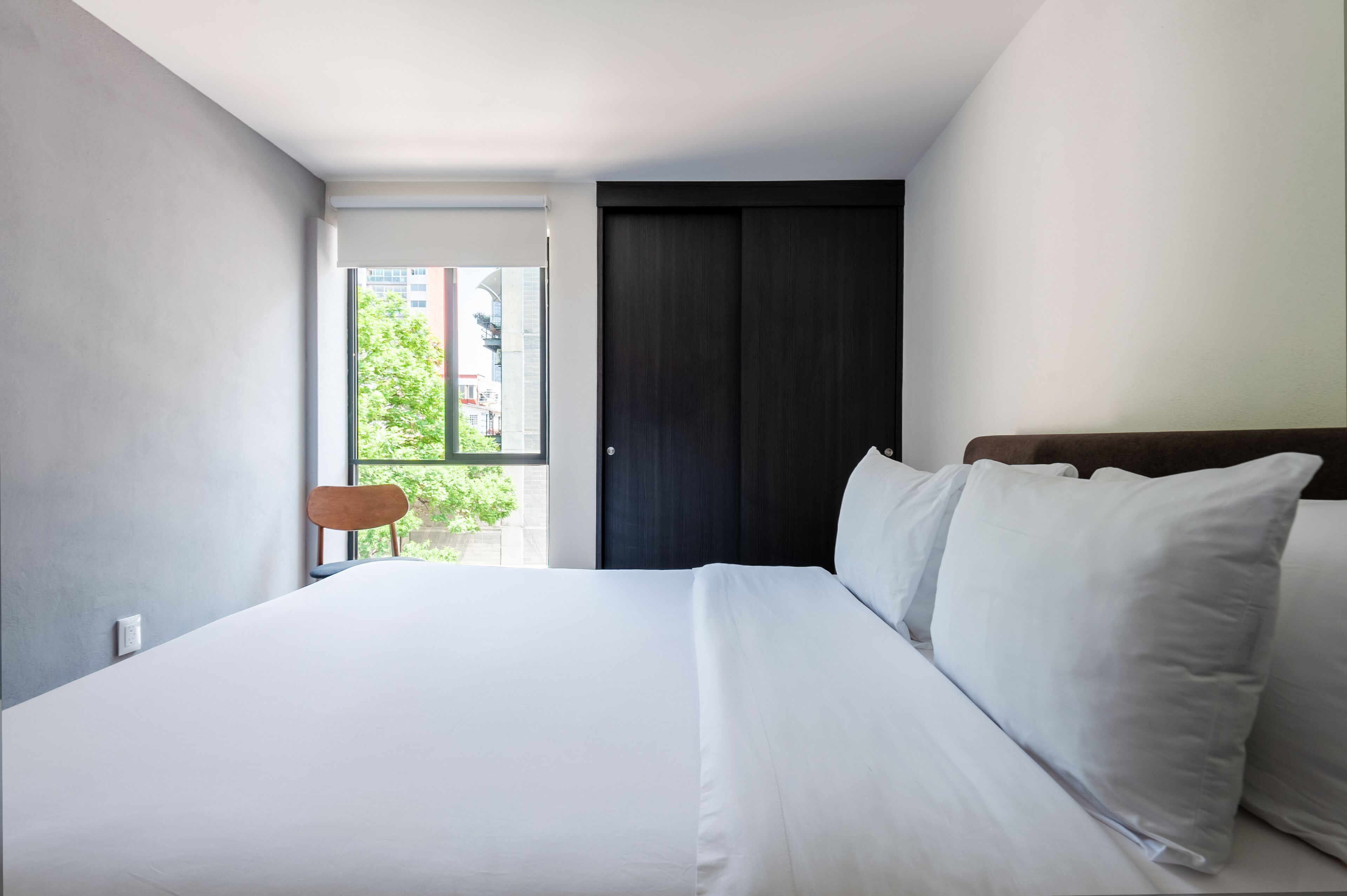 A modern hotel room with a large bed, a dark wooden wardrobe, and a view of greenery outside.