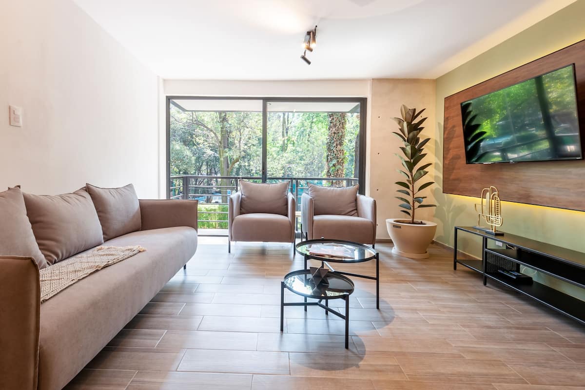 Una sala de estar moderna con un sofá, dos sillones, una mesa de centro y un televisor montado en la pared.