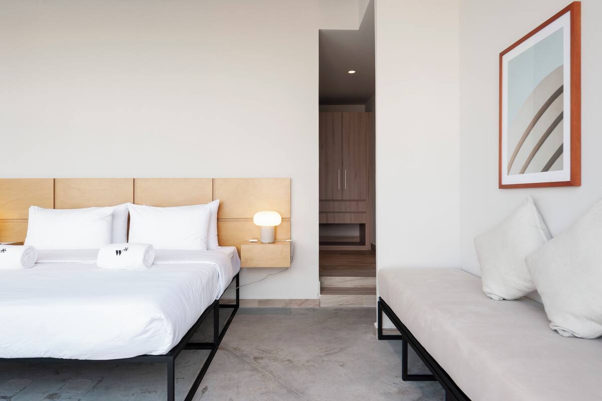 Une chambre d’hôtel moderne, équipée d’un lit, d’un canapé, d’une table de chevet avec une lampe et d’un tableau encadré au mur.