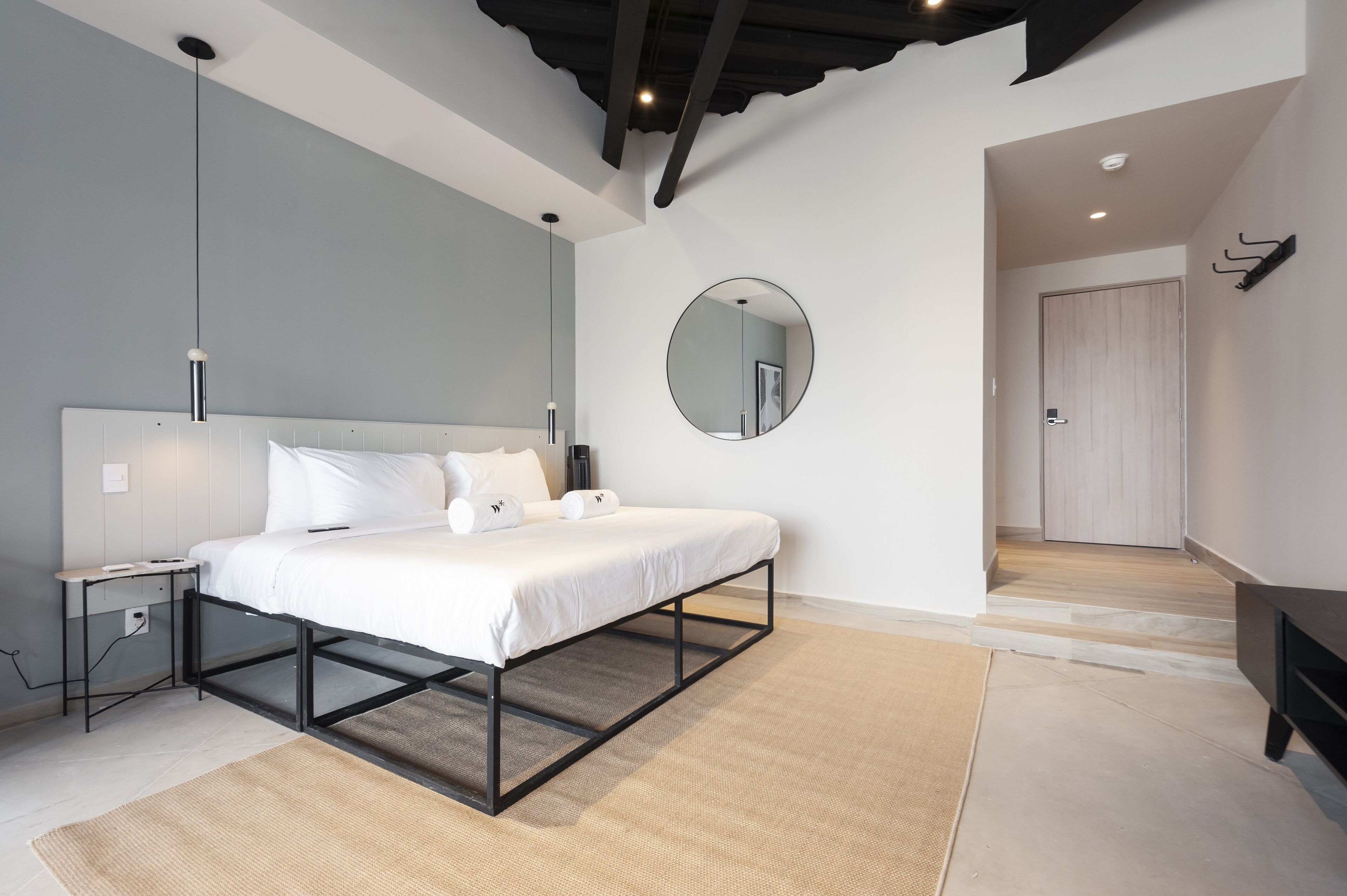 Une chambre à coucher moderne avec un lit, des tables de chevet, un miroir rond et un dressing.
