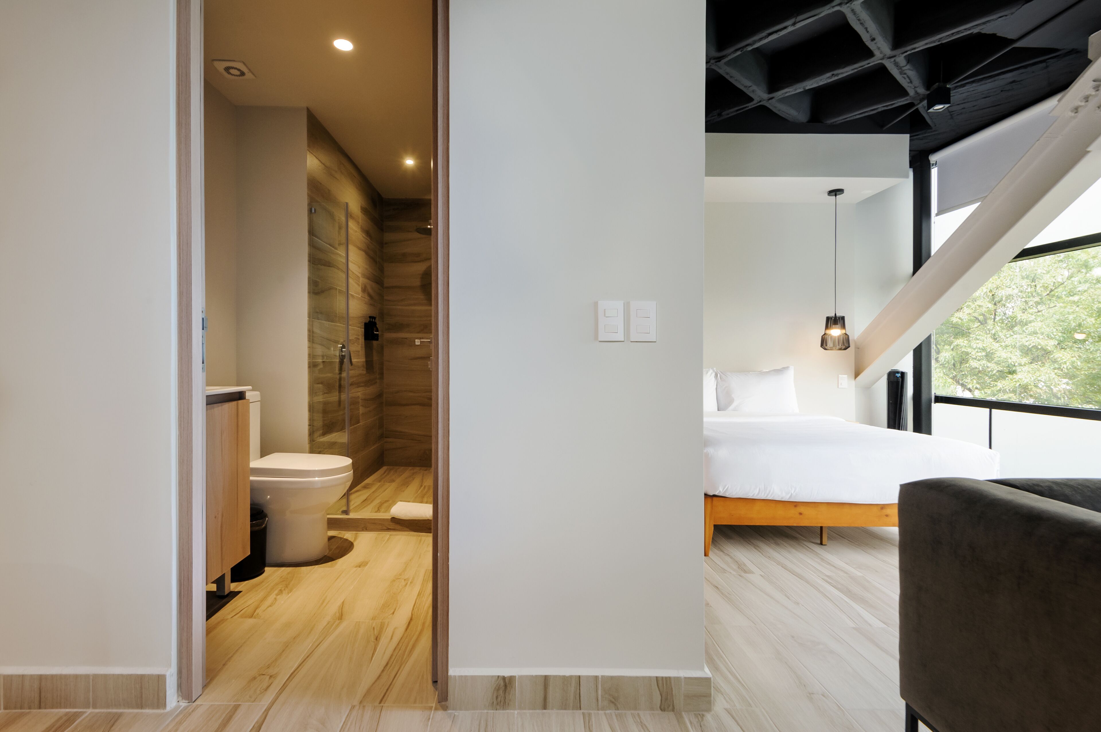 A modern bedroom with a bed, a nightstand, and a window with a view of trees.
